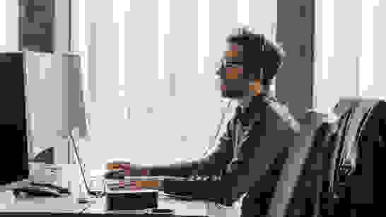 Low Code Mann arbeitet an Low-/No-Code am Laptop, trägt Headset und schaut in Bildschirm