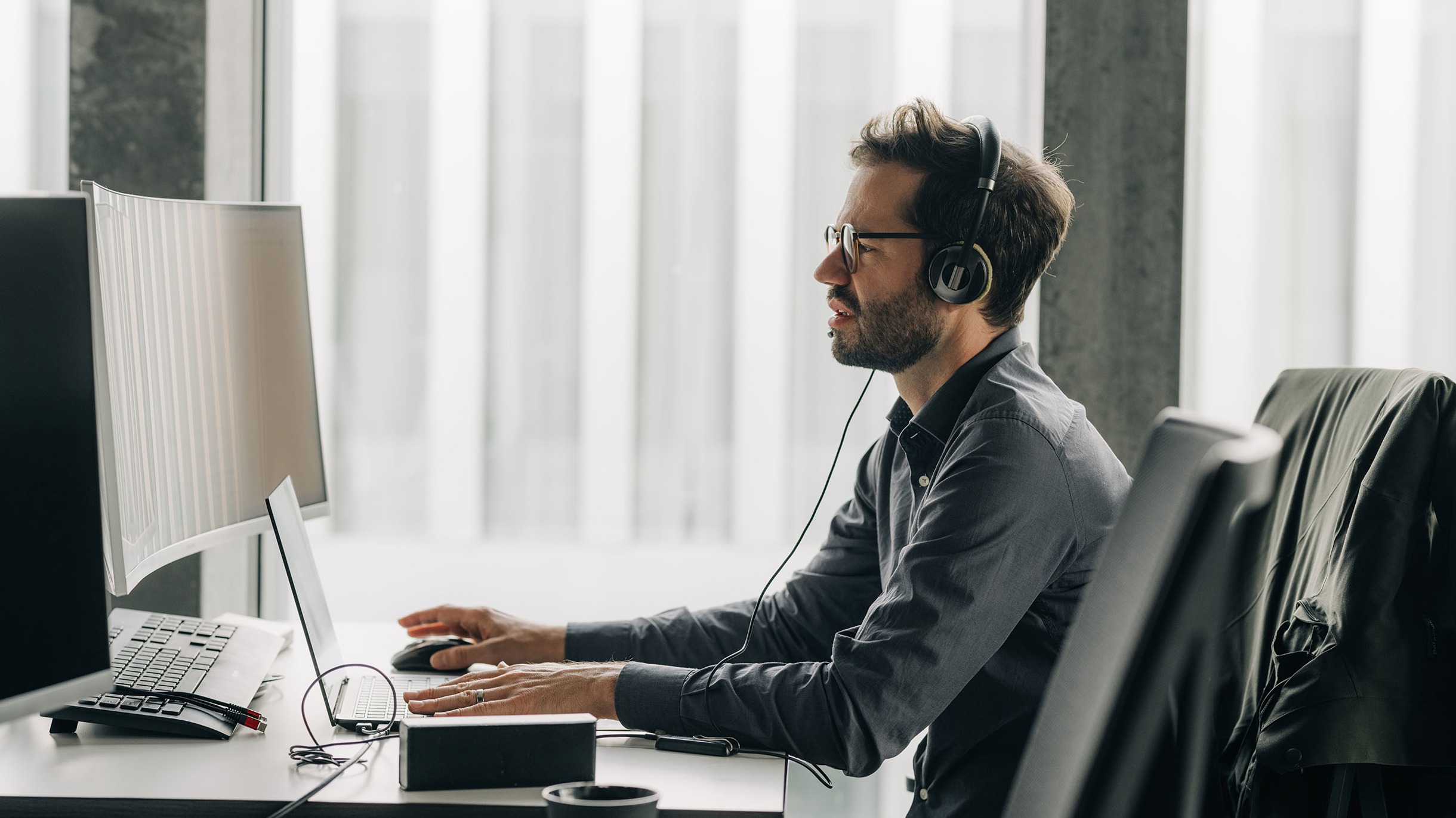 Mann arbeitet an Low-/No-Code am Laptop, trägt Headset und schaut in Bildschirm