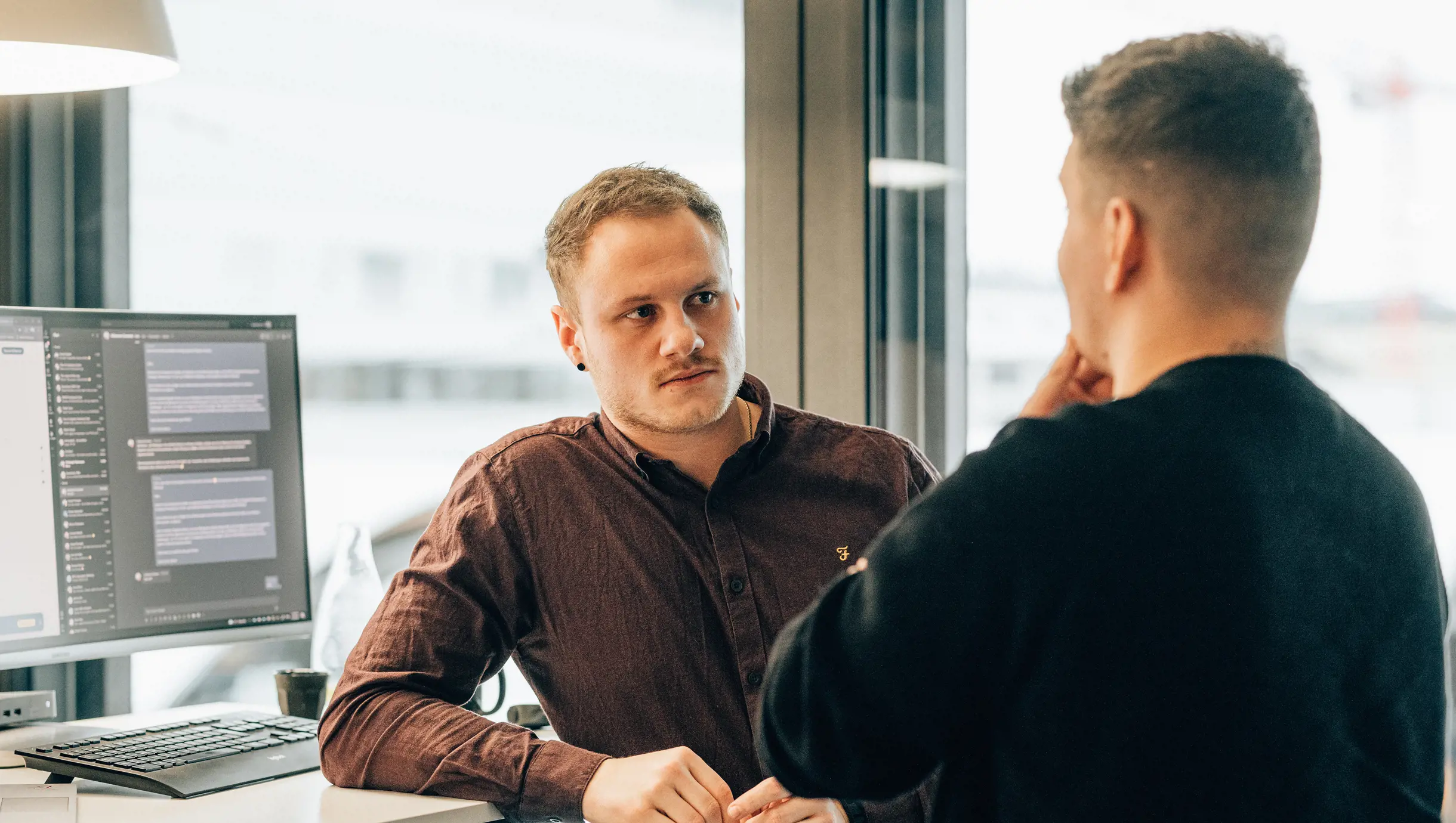 Männlicher Software Engineer in Angular steht mit Mann an Arbeitsplatz und spricht