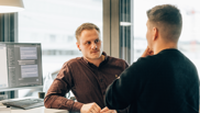 Offene Stelle bei isolutions als Software Engineer in Angular Männlicher Software Engineer in Angular steht mit Mann an Arbeitsplatz und spricht