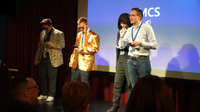 Jahreskickoff 2024 MCS Business Unit Pitches Vier Herren auf der Bühne singen einen Song über ihre Dienstleistung