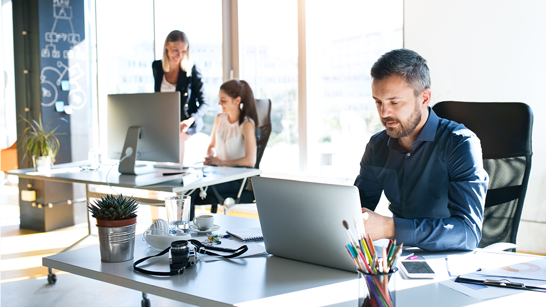 Profond Anlagestiftung Logo Drei Geschäftsleute, die in einem hellen Büro am Laptop arbeiten.