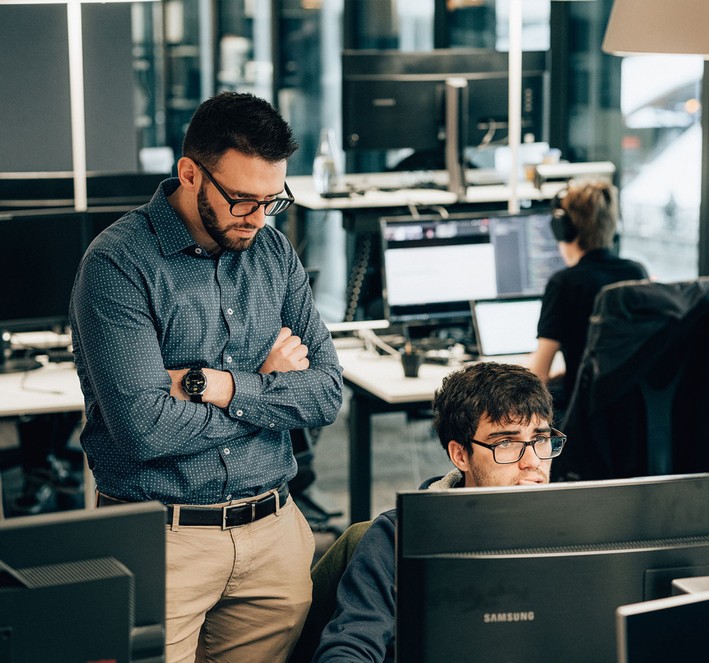 2 Personen vor Computer, eine sitzen eine stehend, prüfen Operation Safety