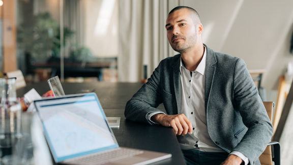 Offering Subscription Microsoft 365 Update Mann an einem Sitzungstisch nach vorne schauend mit offenem Laptop vor sich