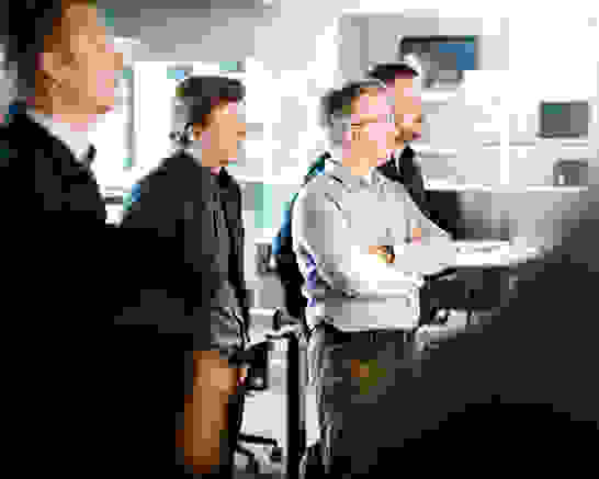 Enterprise Operations Innovation Stehende Männer in einem Büro hören einem Vortrag zu