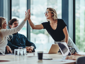 AI driven Employee Experience  Zwei Frauen klatschen sich ab und lachen in einem Meetingraum