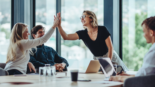 AI driven Employee Experience  Zwei Frauen klatschen sich ab und lachen in einem Meetingraum