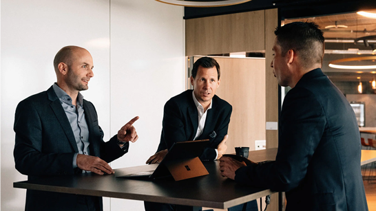 Microsoft Lizenzierung verstehen Drei Herren am Hochtisch über Business am diskutieren.