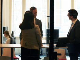 MLL Evaluationsberatung Drei Personen stehen und reden in einem Sitzungszimmer