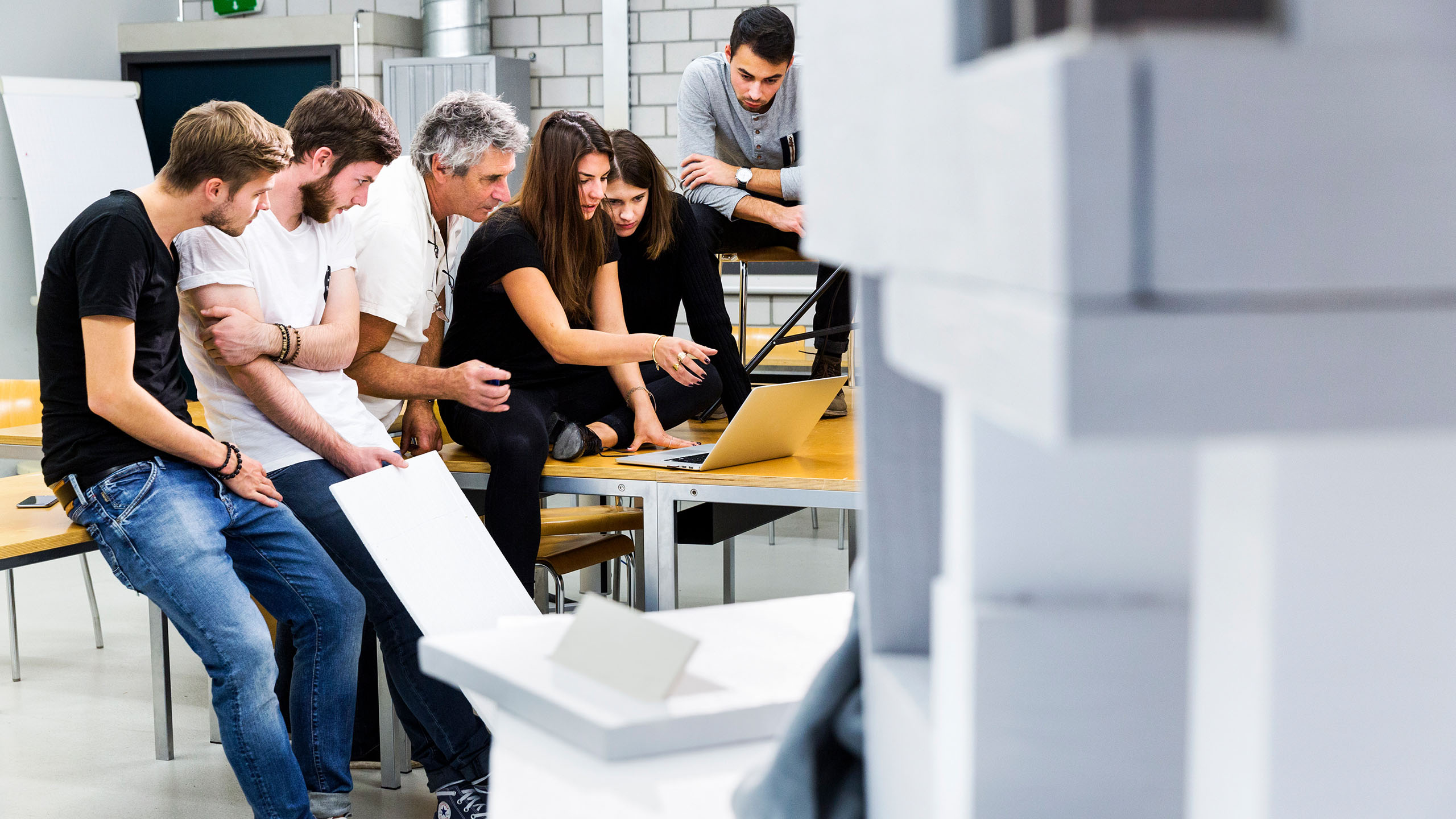 Studierende sitzen zusammen, schauen in Laptop und besprechen etwas