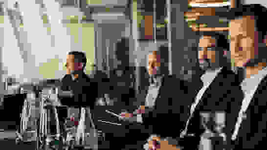 Sitzungszimmer mit 4 Teilnehmenden Männern in Anzug