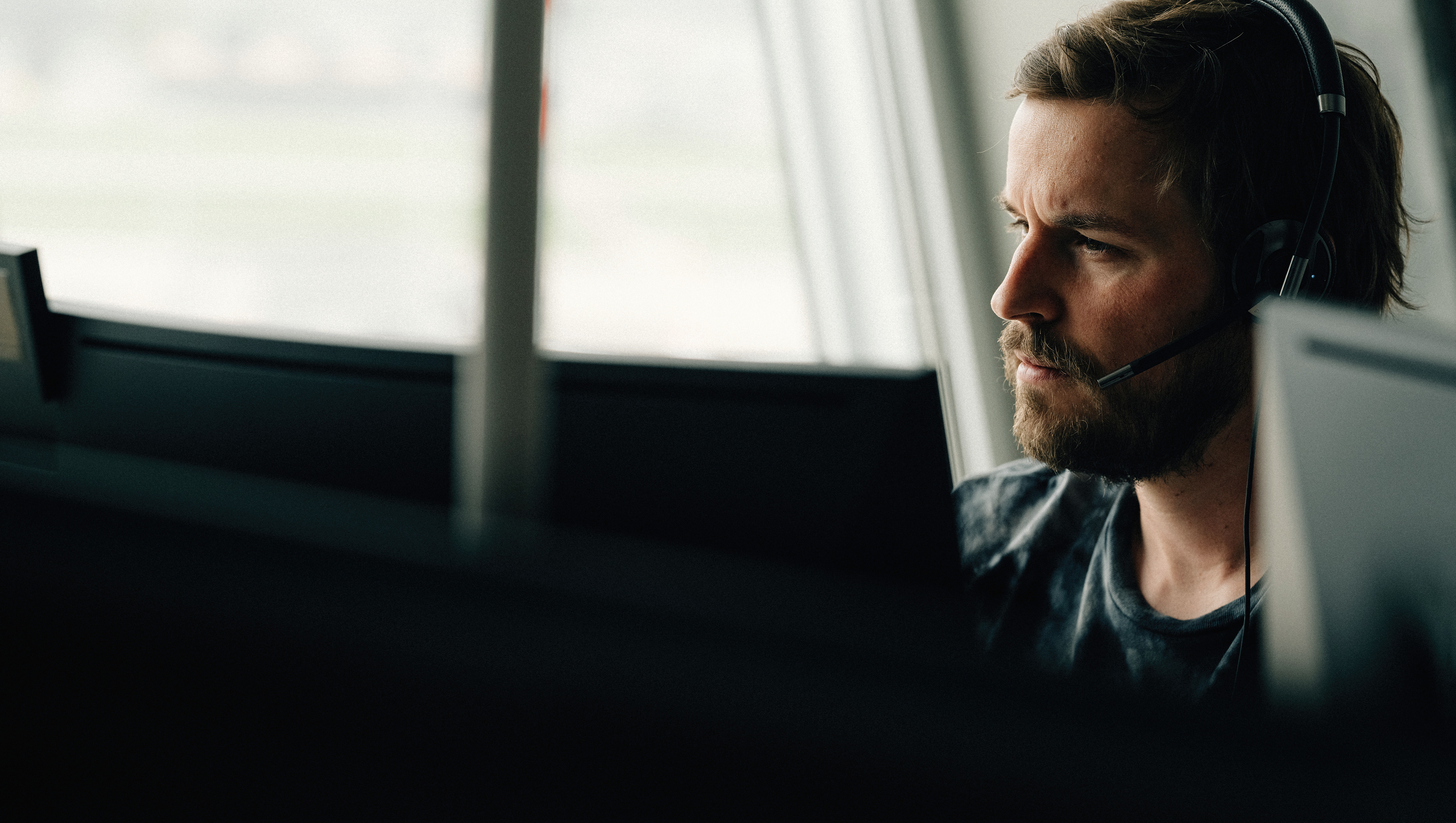 Männlicher Informatiker in Applikationsentwicklung sitzt mit Headset vor PC Bildschirm