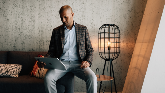 isolutions Whitepaper Microsoft Viva Junger Mann sitzt am Rande eines Sofas und schaut in seinem PC rein