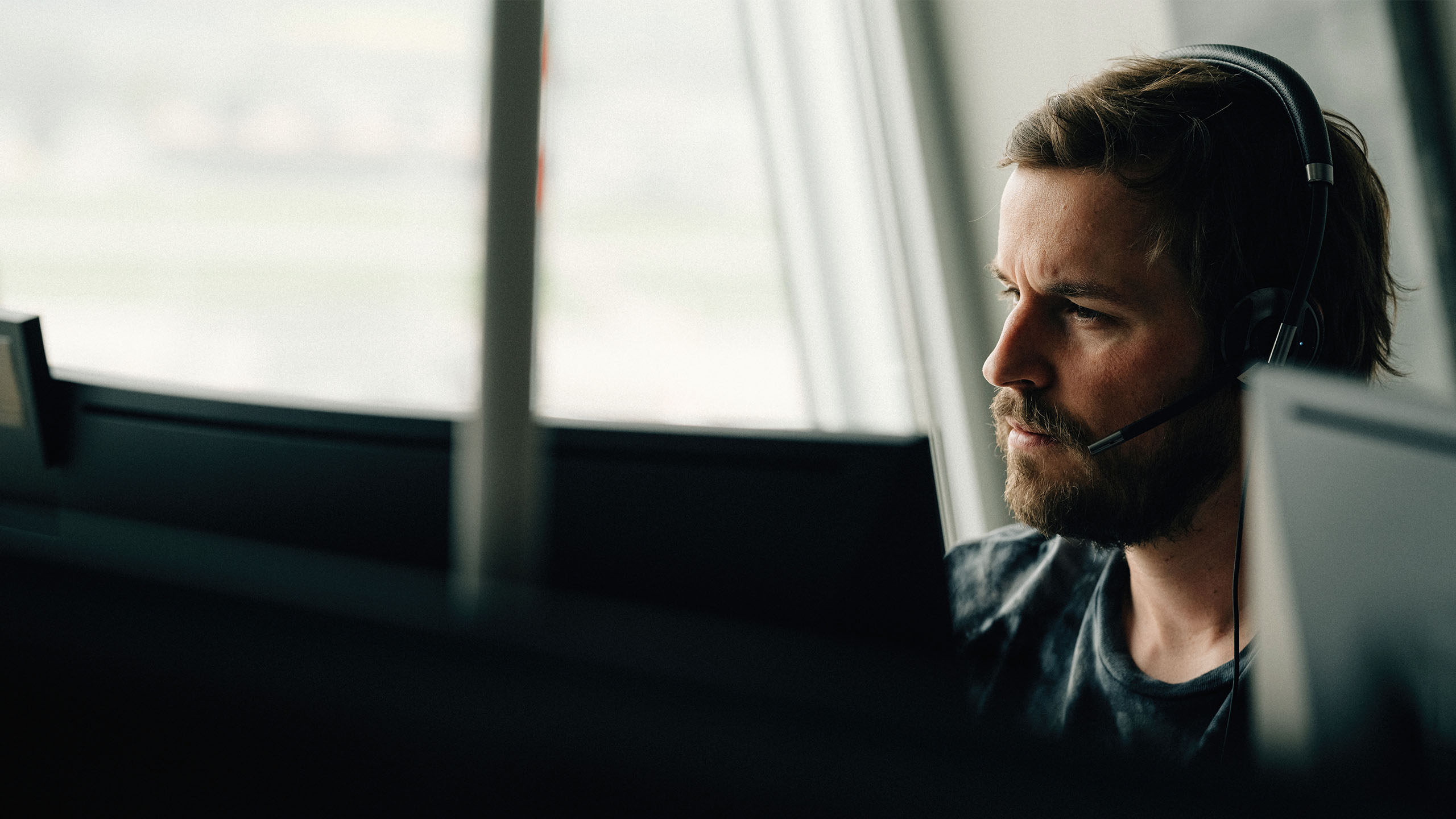 Frontansicht von jungem Mann am PC mit Headset schaut Data Analytics/Power BI an