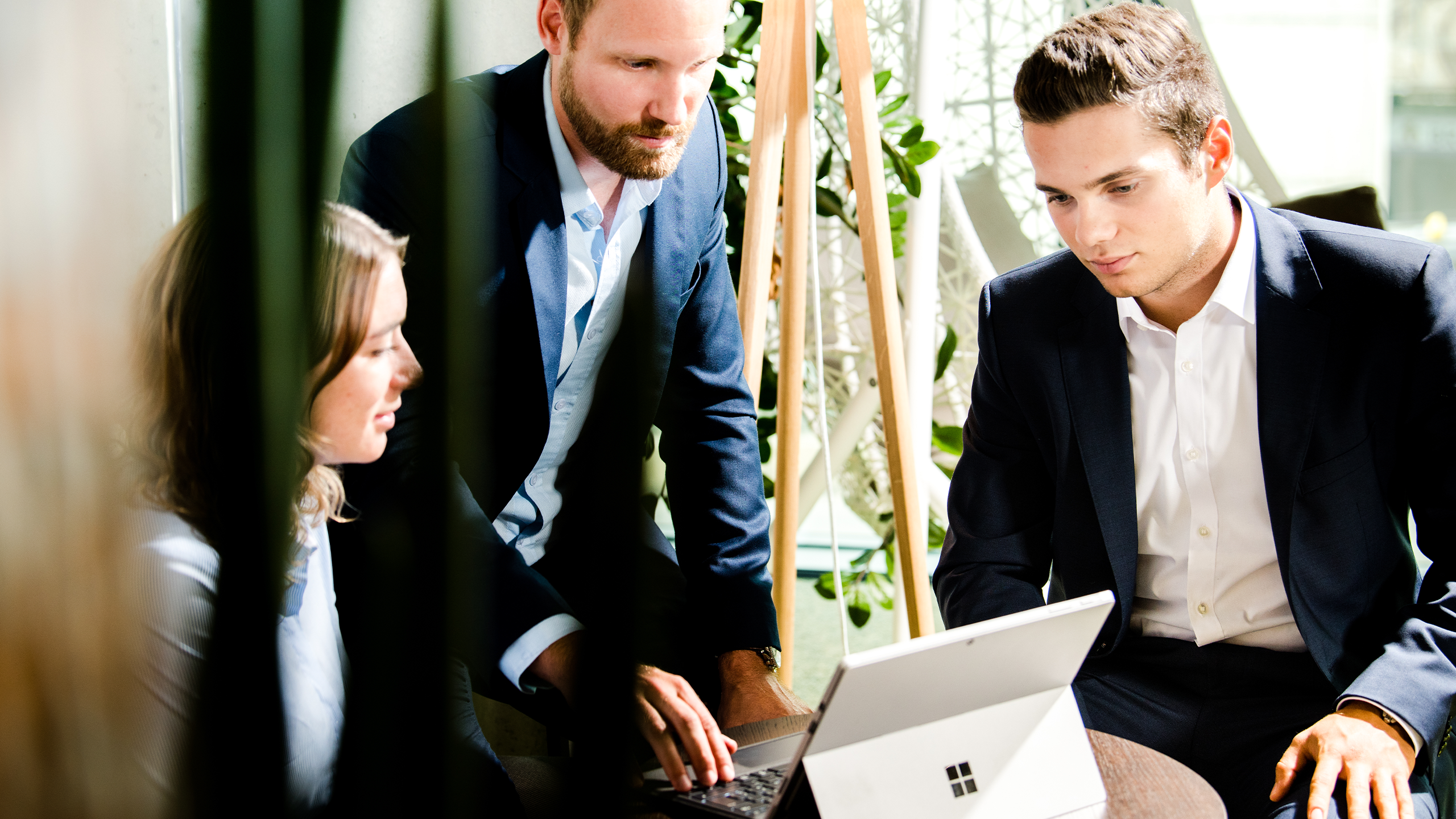Drei Personen im Anzug sitzen um einen Laptop