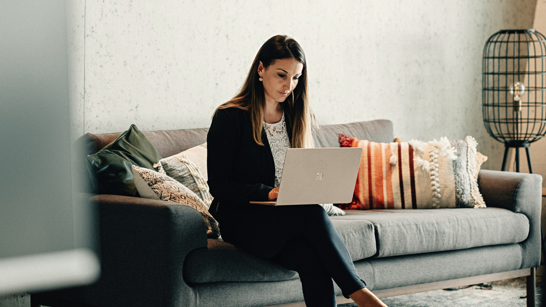 Frau sitz auf einem Sofa mit dem Laptop auf dem Schoss