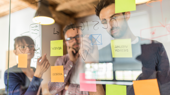 Personen in einem Workshop arbeiten mit Post It Wand