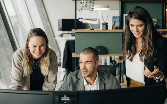Offene Stelle als Digital Marketing Manager Zwei weibliche und ein männlicher Digital Marketing Manager diskutieren vor PC Bildschirm