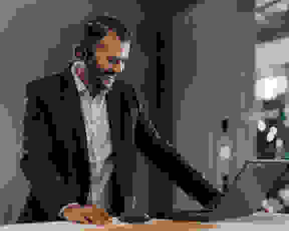 Digital Sales - Acceleration Of Processes Digital Sales: Junger lachender Mann mit Headset telefoniert am Laptop