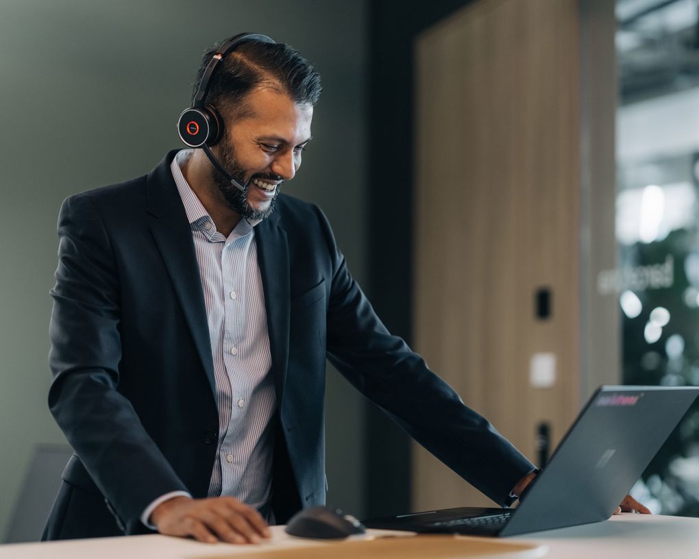Digital Sales: Junger lachender Mann mit Headset telefoniert am Laptop