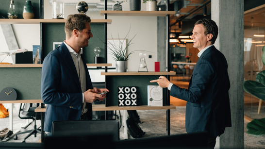 isolutions Whitepaper Employee Experience Zwei junge Männer stehen im Gang des Offices und lachen sich an