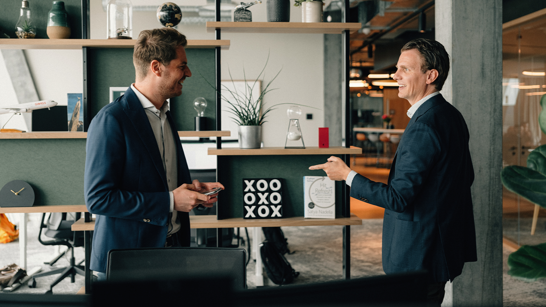 Zwei junge Männer stehen im Gang des Offices und lachen sich an