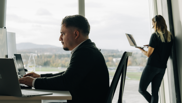 Offene Stelle bei isolutions als Microsoft 365 Architect Security Compliance Frau steht telefonierend am Fenster und männlicher Microsoft 365 Architect sitzt im Vordergrund an PC