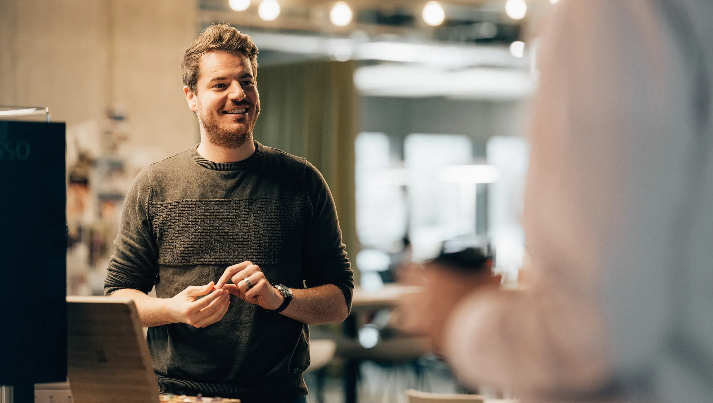 Männlicher Digital Business mit EFZ steht vor Kaffeemaschine und lacht