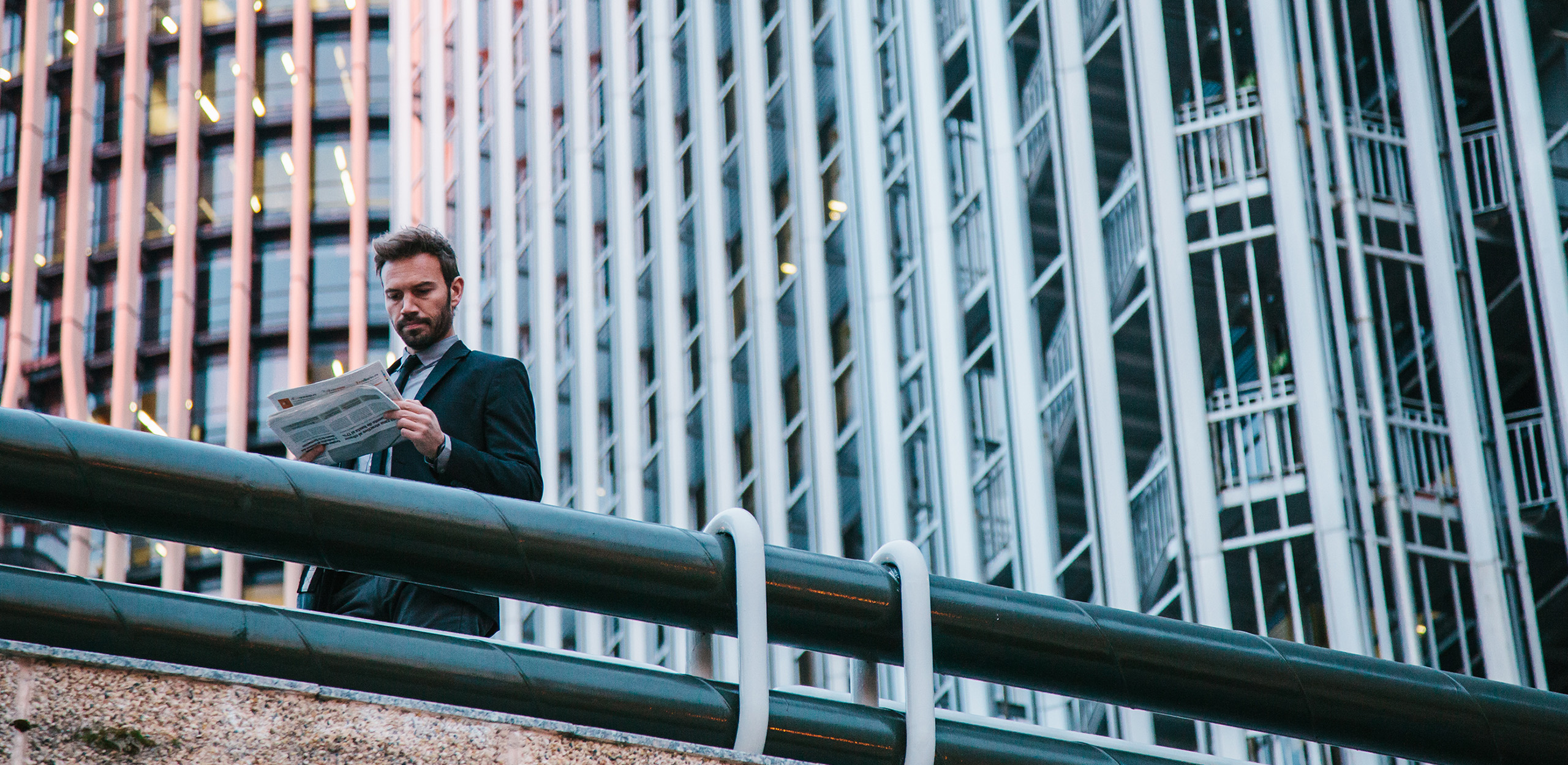 Mann im Anzug liest eine Zeitung auf einer Brücke