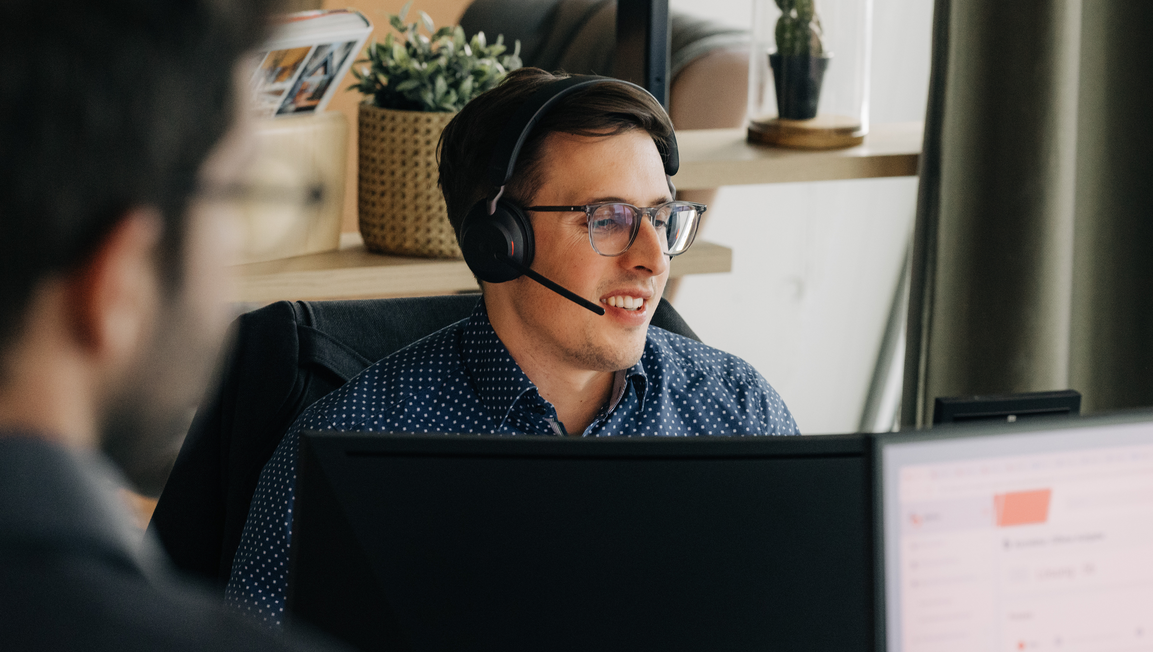 Männlicher Technical Consultant sitzt mit Headset vor PC Bildschirm