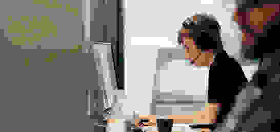 Lehrling mit schwarzem Shirt am arbeiten mit Headset und am Computer