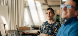 App Modernization Package Engage Frau in Sitzungszimmer schaut nach vorne, rechts unscharf lachender Mann