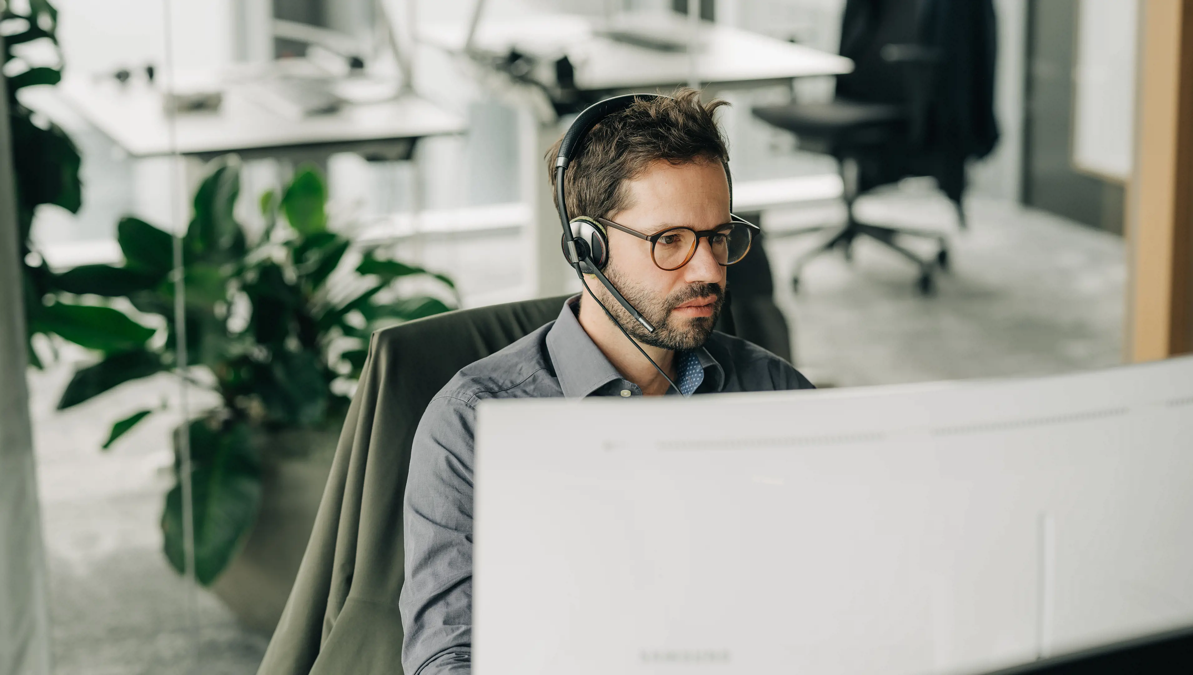 Männlicher Support Engineer sitzt mit Headset vor PC Bildschirm