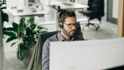 Offene Stelle bei isolutions als Support Engineer Männlicher Support Engineer sitzt mit Headset vor PC Bildschirm