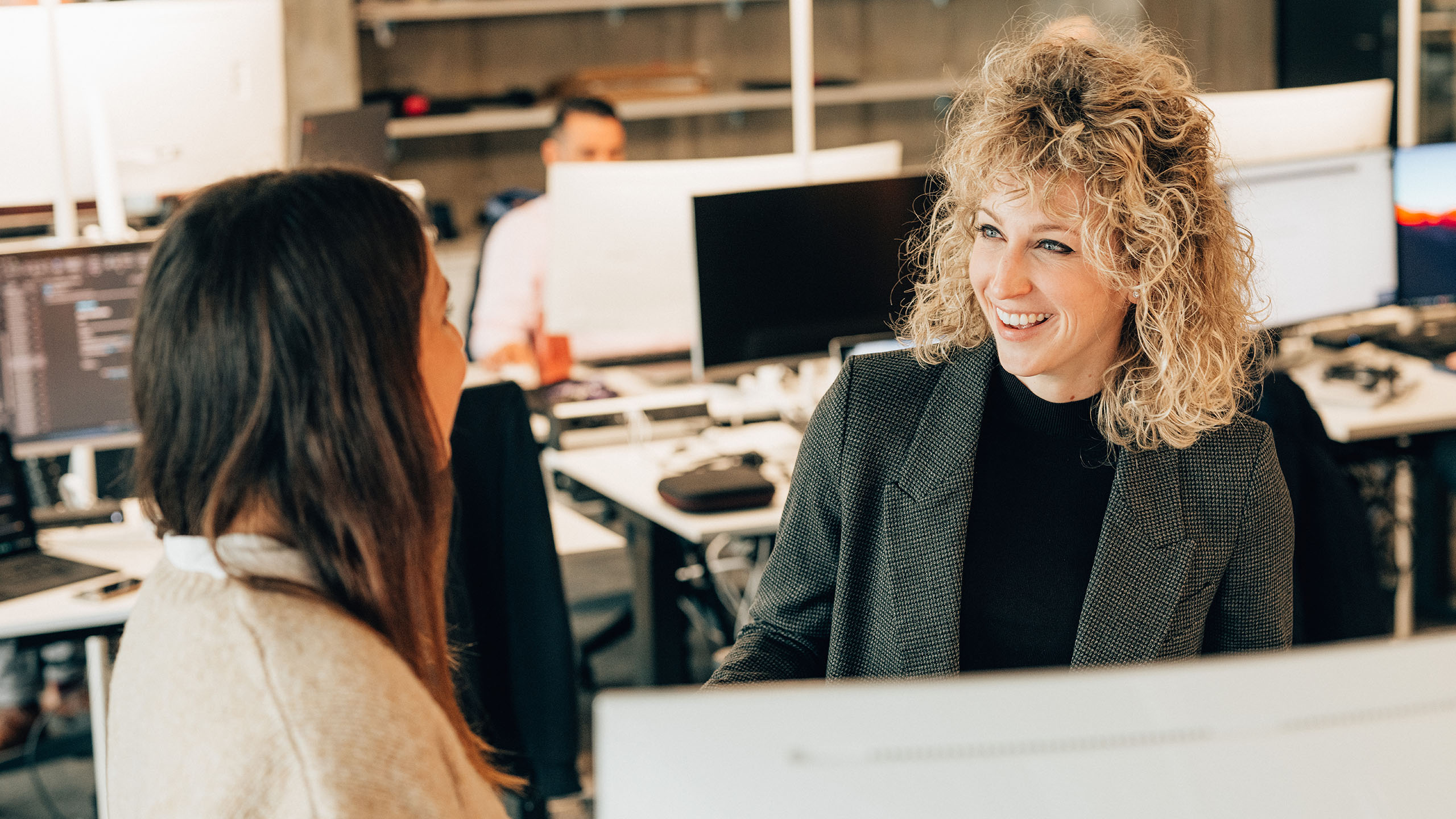 2 Frauen vor PC, eine am Lachen, besprechen Angebote für Customer Services