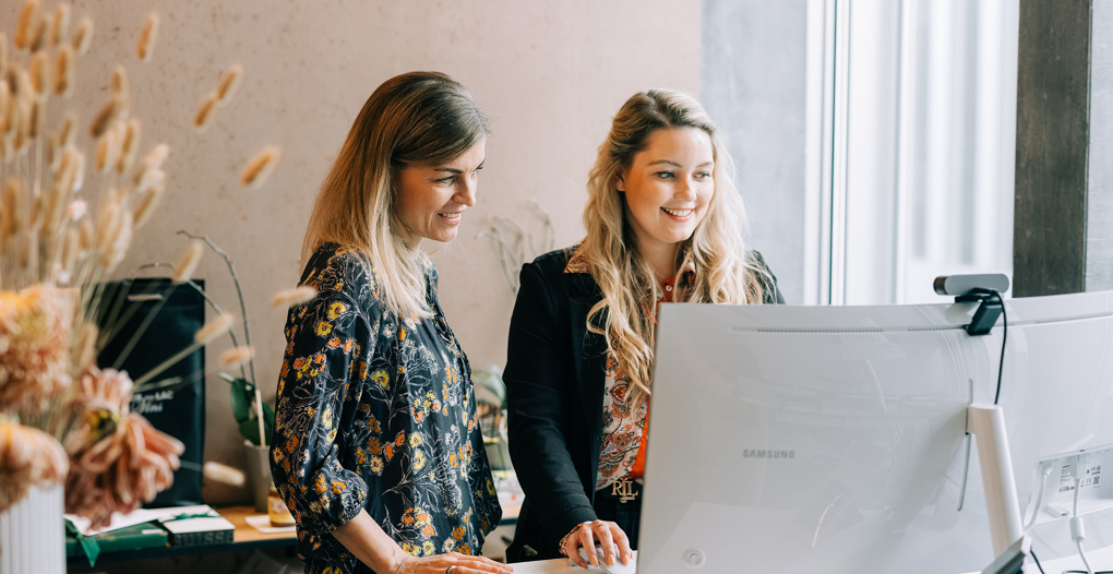 2 stehende Frauen vor PC zur Besprechung der CRM Consulting